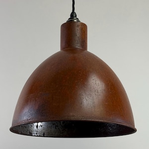 May include: A vintage-style pendant light with a rusty brown, dome-shaped shade. The light fitting has a cylindrical top and a black cord. The interior of the shade is a darker, mottled colour. It hangs against a white backdrop.