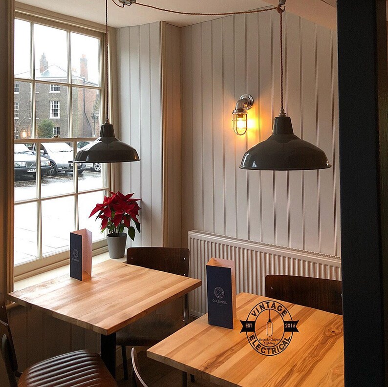 Puede incluir: Interior de un caf&eacute; con dos mesas y sillas de madera. Dos l&aacute;mparas colgantes grises cuelgan del techo. Una ventana ofrece una vista del exterior. Una flor de pascua roja est&aacute; en el alf&eacute;izar.
