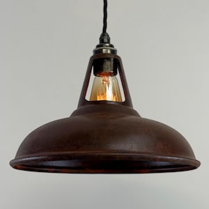 May include: A rustic, brown metal pendant light with a domed shade and exposed bulb. The light fixture has a vintage industrial design, with a dark, weathered finish and a black cord. The bulb is a warm, amber color.
