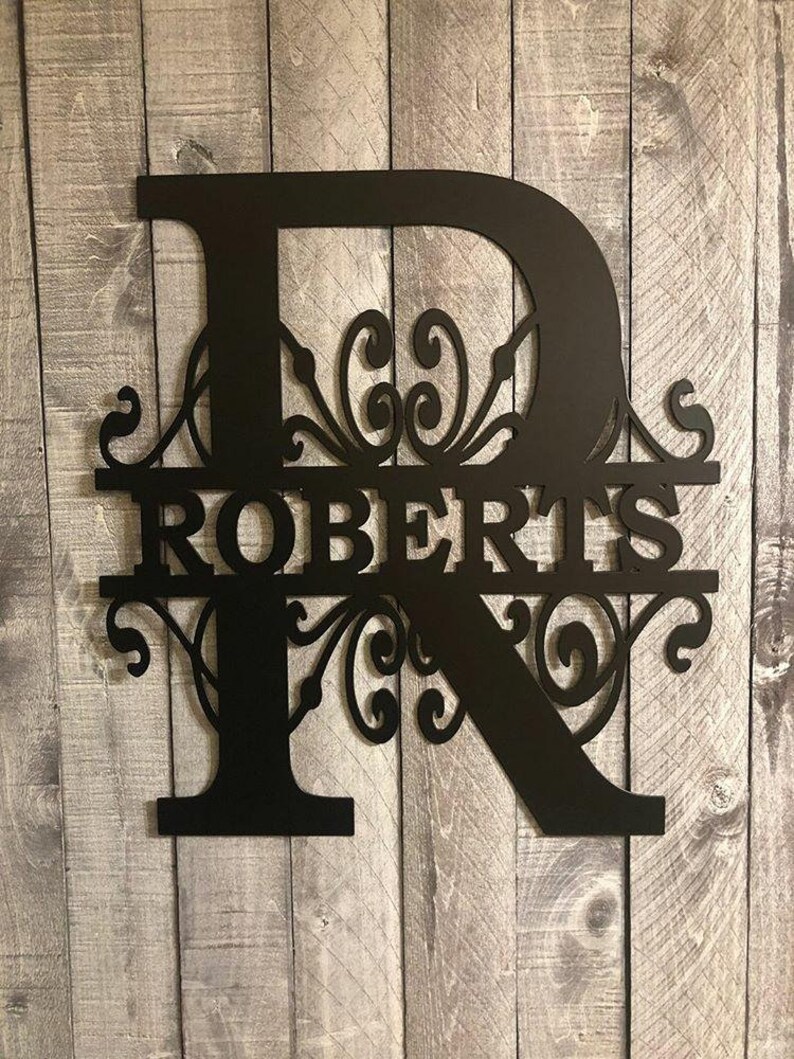 K&ouml;nnte beinhalten: Schwarzes Metallmonogramm mit dem Buchstaben "R" und dem Namen "ROBERTS" in einer dekorativen Schriftart. Der Buchstabe "R" hat ein dekoratives Schn&ouml;rkeldesign.