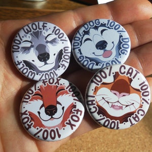 Könnte beinhalten: Vier runde Knöpfe mit Tiergesichtern und Text um den Rand. Die Knöpfe sind weiß mit schwarzem Text und zeigen einen Wolf, einen Hund, eine Katze und einen Fuchs.