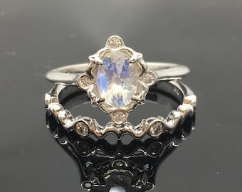 May include: A silver ring set with a large oval moonstone surrounded by smaller clear stones. The ring is set on a delicate band with a scalloped edge and smaller clear stones.
