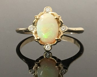 May include: A gold ring with an oval opal gemstone surrounded by small diamonds. The ring has a delicate, ornate design.