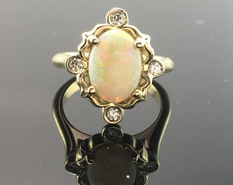 May include: A gold ring with an oval opal gemstone surrounded by small diamonds. The ring has a delicate, ornate design.