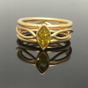 May include: A gold ring with a yellow marquise-shaped gemstone set in the center. The ring is made of three bands that are intertwined.