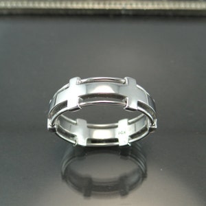 May include: A silver-colored ring with a unique design. The ring features a series of rectangular and curved elements, creating an open, geometric pattern. The band is smooth and polished, reflecting light. The ring is marked with "14K".