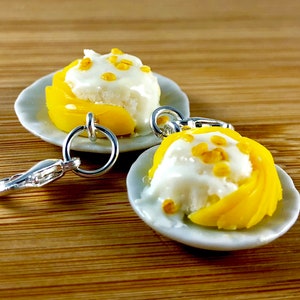 May include: Miniature dessert charms featuring a white cream topping with yellow fruit slices, and small yellow sprinkles, on a white plate. The charms are attached to a silver-colored keychain ring.