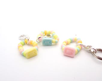 May include: Three charm bracelets with pastel-coloured beads and rectangular centrepieces in yellow, blue, and pink. A silver clasp is attached to one bracelet, suggesting they can be used as keychains or jewellery.