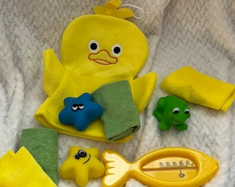 Puede incluir: Un conjunto de juguetes de baño amarillos y verdes, que incluyen un guante de baño con forma de pato, un termómetro con forma de pez, dos estrellas de mar, una rana y toallitas. Dispuestos sobre una superficie blanca texturizada.