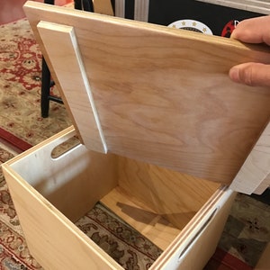 Puede incluir: Una caja de madera con una tapa con bisagras. La tapa est&aacute; abierta y la caja est&aacute; vac&iacute;a. La caja est&aacute; hecha de madera clara y tiene un acabado natural.