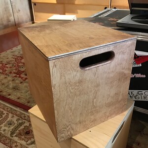 Puede incluir: Una caja de madera con un asa en la parte superior. La caja est&aacute; hecha de madera marr&oacute;n claro y tiene un acabado natural. La caja est&aacute; colocada encima de otra caja de madera.