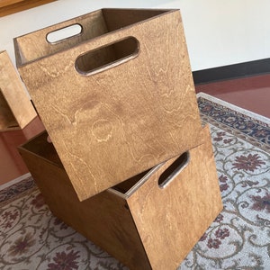 May include: Two wooden storage boxes with handles. The boxes are stacked on top of each other. The boxes are made of light brown wood and have a natural finish.