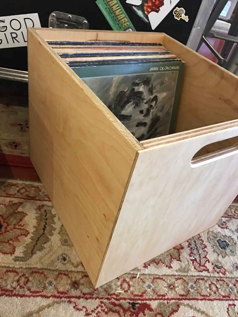 Puede incluir: Una caja de almacenamiento de madera para discos de vinilo con un asa recortada. La caja est&aacute; llena de discos de vinilo, incluyendo uno con el t&iacute;tulo "JAPAN OIL ON CANVAS".