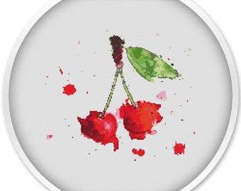 Puede incluir: Un diseño de punto de cruz de dos cerezas rojas brillantes con tallos verdes y una hoja. Las cerezas tienen un efecto de acuarela con salpicaduras de pintura roja. El diseño está en un marco circular blanco.
