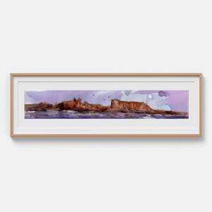 May include: A panoramic watercolor landscape painting in a light wood frame. The artwork depicts a rugged brown cliffside coastline against a soft purple sky, with dark water below and small birds flying in the distance above the horizon line.