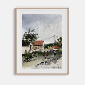 May include: Watercolor painting of a rural scene with houses, trees, and figures. The houses have red tile roofs. Clothes hang on a line. The artwork is framed in a light brown wooden frame.
