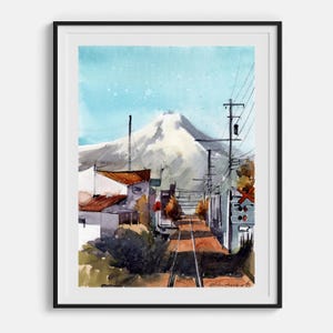 May include: Watercolor painting of a mountain landscape with a railway track. The artwork features a snow-capped mountain, buildings, and power lines under a blue sky. The painting is framed in a black border.