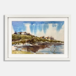 Könnte beinhalten: Ein Aquarell-Landschaftsgemälde in einem weißen Rahmen, das einen grasbewachsenen Hügel mit kleinen Häusern, ein spiegelndes Gewässer im Vordergrund und einen blauen Himmel mit weichen, vertikalen Farbwäschen zeigt, die Regen oder Licht andeuten.