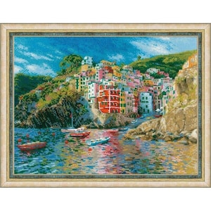 May include: Framed cross-stitch artwork depicting a colorful coastal village scene. The artwork features a vibrant array of buildings in shades of red, yellow, and pink, set against a backdrop of blue water and sky. Small boats dot the water.