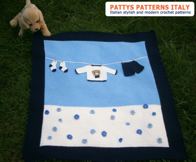 Puede incluir: Una manta de beb&eacute; hecha a mano con un dise&ntilde;o azul y blanco, con un tendedero con ropa de ganchillo en miniatura. La manta tiene un borde azul marino y est&aacute; decorada con aplicaciones de flores azules. El texto "PATTY'S PATTERNS ITALY" es visible.
