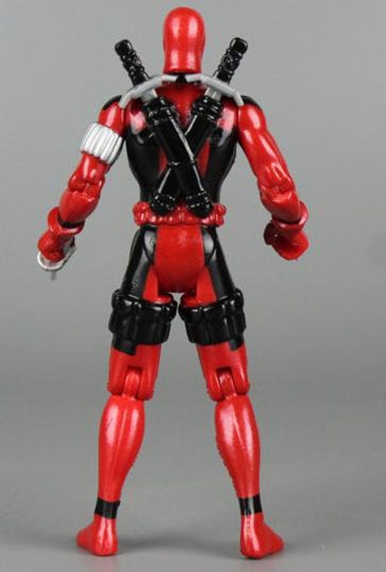May include: A red and black action figure of Deadpool with a black mask and a red and black suit. The figure is holding two swords in its back.