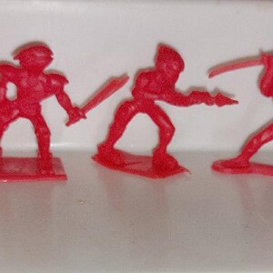 May include: Set of seven red plastic toy figures, each with a different pose and weapon. The figures are all about 2 inches tall and are made of a bright red plastic.