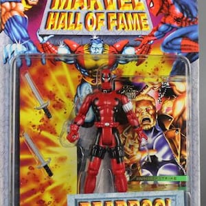 May include: A red and black action figure of Deadpool from the Marvel Hall of Fame series. The figure is holding two swords and is standing on a base with the word "DEADPOOL" printed on it.