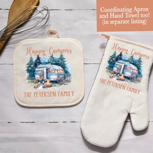May include: Off-white pot holder and oven mitt featuring a watercolor design of a vintage camper, campfire, and trees. The text "Happy Campers" and "THE PETERSEN FAMILY" are printed on both items. A wooden whisk is in the background.