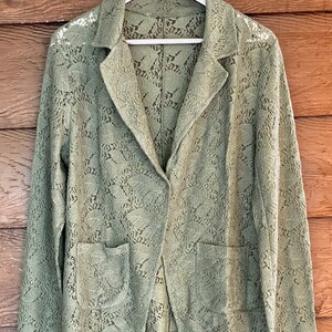 May include: A green lace blazer with a button closure and two pockets. The blazer is made of a delicate, lightweight fabric and has a relaxed fit.