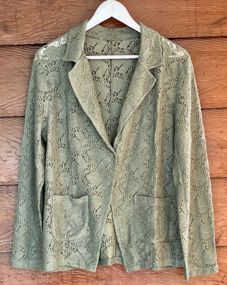 May include: A green lace blazer with a button closure and two pockets. The blazer is made of a delicate, lightweight fabric and has a relaxed fit.