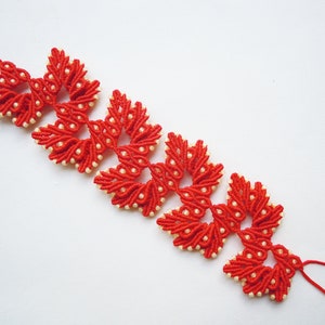 May include: A red and white beaded bracelet with a knotted design. The bracelet is made of small red beads and white beads, and the knots are arranged in a pattern of flowers.