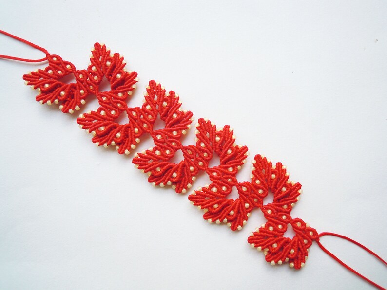 May include: A red and white beaded bracelet with a knotted design. The bracelet is made of small red beads and white beads, and the knots are arranged in a pattern of flowers.