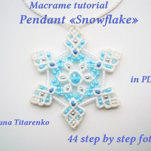 Puede incluir: Pendiente de copo de nieve de macramé blanco con cuentas azules y plateadas. El pendiente está sobre un fondo blanco con el texto "Macrame tutorial Pendant «Snowflake» in PDF Yuna Titarenko 44 step by step foto".