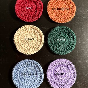 May include: Six crocheted coasters in different colours and patterns. The colours are wine, bruschetta, cream, forest, stonewash, and amethyst. The coasters are all round and have a raised centre.
