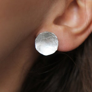 Peut inclure: Une paire de boucles d'oreilles en argent avec une texture martelée. Les boucles d'oreilles sont rondes et ont une forme légèrement irrégulière.