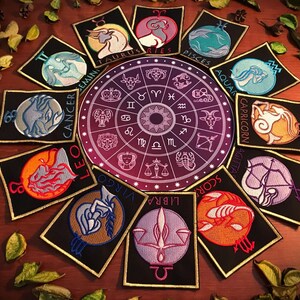 Peut inclure: Un ensemble de 12 patchs du zodiaque, chacun représentant un symbole astrologique différent et un design coloré. Les patchs sont disposés en cercle autour d'une roue zodiacale centrale.
