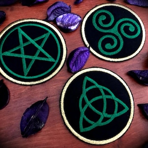 Può includere: Tre toppe rotonde ricamate con tessuto nero e ricamo verde. Le toppe presentano un pentagramma, un triskelion e un triquetra.