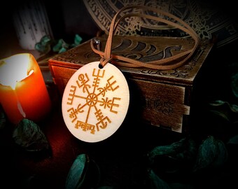 May include: A wooden pendant with a Vegvisir symbol, a Norse compass, engraved on it. The pendant is hanging from a brown leather cord and is resting on a wooden box.