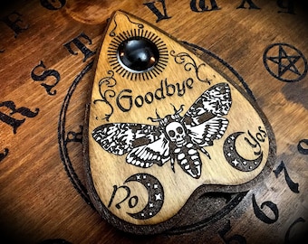May include: Wooden planchette with a black and white moth design, a skull, and the words "Goodbye", "Yes", and "No".
