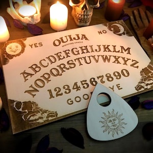 Può includere: Un tabellone Ouija in legno con una planchette con un design a forma di sole. Il tabellone ha l'alfabeto, i numeri da 1 a 9 e lo 0, e le parole "sì", "no" e "arrivederci".