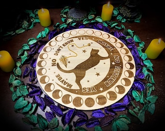 May include: A wooden Ouija board with a black cat design and the words "Yes", "Maybe", "No", and "Don't Know" around the edge. A gold pendulum hangs in the centre of the board.