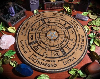 Puede incluir: Una rueda de madera con un pentagrama plateado en el centro. La rueda está dividida en ocho secciones, cada una con un nombre y un rango de fechas diferente. Los nombres son: Yule, Imbolc, Ostara, Beltane, Litha, Lammas, Mabon y Samhain. Las fechas son: 20-23 de diciembre, 2 de febrero, 20-23 de marzo, 30 de abril, 20-23 de junio, 1 de agosto, 20-23 de septiembre y 31 de octubre.