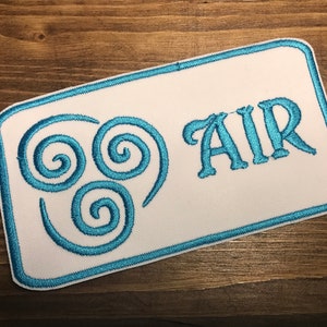 May include: A white embroidered patch with a blue outline. The patch features the Air Nation symbol, three blue interlocking spirals, and the word "AIR" in blue lettering.