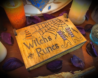Puede incluir: Caja de madera con un diseño de sombrero de bruja, telaraña y botas de bruja. La caja está etiquetada "Witch's Runes".