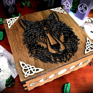 Op de afbeelding: Houten doos met een zwart wolfontwerp op de deksel. De doos heeft een Keltisch knoopontwerp op de hoeken en een wit interieur.