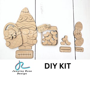 May include: DIY craft kit featuring a gnome holding a basket of Easter eggs, a jar of jelly beans with a "Bunny Bait" tag, and a stack of Easter eggs. The kit is made of unfinished wood and is ready to be painted.