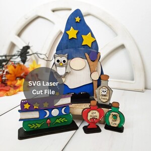 Könnte beinhalten: Ein Holz-Zwerg mit einem blauen Zaubererhut mit gelben Sternen, der einen Stab und eine Eule hält. Der Zwerg steht auf einem Stapel Bücher mit Monden und Sternen. Es gibt drei Flaschen mit Tränken mit den Etiketten: "Tödliches Gift", "Liebestrank" und "Glückselixier".