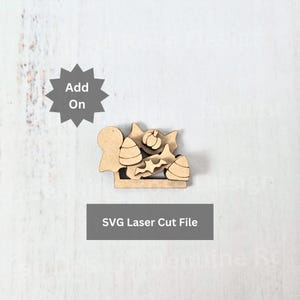 May include: A light brown laser-cut wooden shape featuring a ghost, candy corn, a pumpkin, and a bat. Above the shape is a dark gray starburst icon with the text Add On. Below the shape is a dark gray rectangle with the text SVG Laser Cut File.