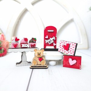 Pode incluir: Decora&ccedil;&otilde;es de madeira para o Dia dos Namorados, incluindo uma caixa de correio vermelha com as palavras "Sending Love", um urso de peluche a segurar um cora&ccedil;&atilde;o, cupcakes com cora&ccedil;&otilde;es e XO, e envelopes com cora&ccedil;&otilde;es.