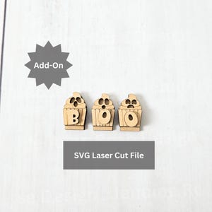May include: Three wooden cupcake-shaped cutouts spelling "BOO" for Halloween. The cutouts are light brown with a cupcake design and the letters are visible. The image also includes the text "SVG Laser Cut File" and "Add-On".